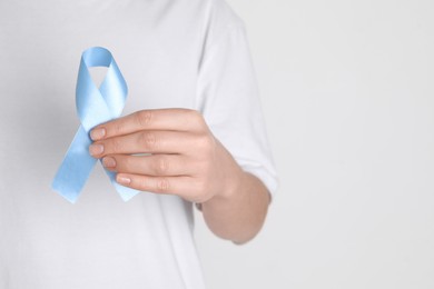 Photo of International Psoriasis Day. Woman with light blue ribbon as symbol of support on white background, closeup. Space for text