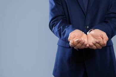 Businessman holding something on grey background, closeup view of hands with space for text