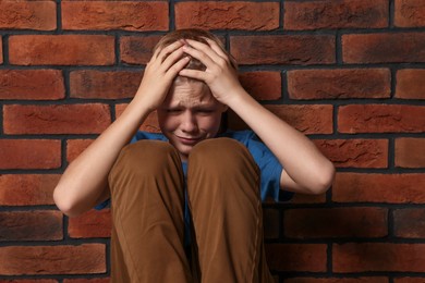 Photo of Upset boy sitting near brick wall. Children's bullying