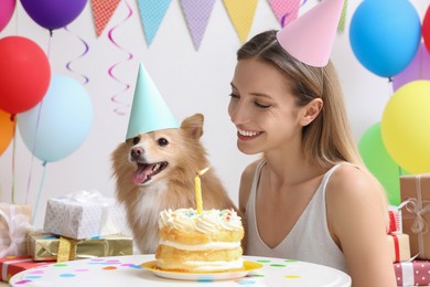 Photo of Happy woman celebrating her pet's birthday in decorated room
