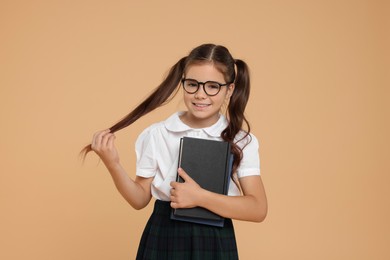 Photo of Cute schoolgirl in glasses with books on beige background