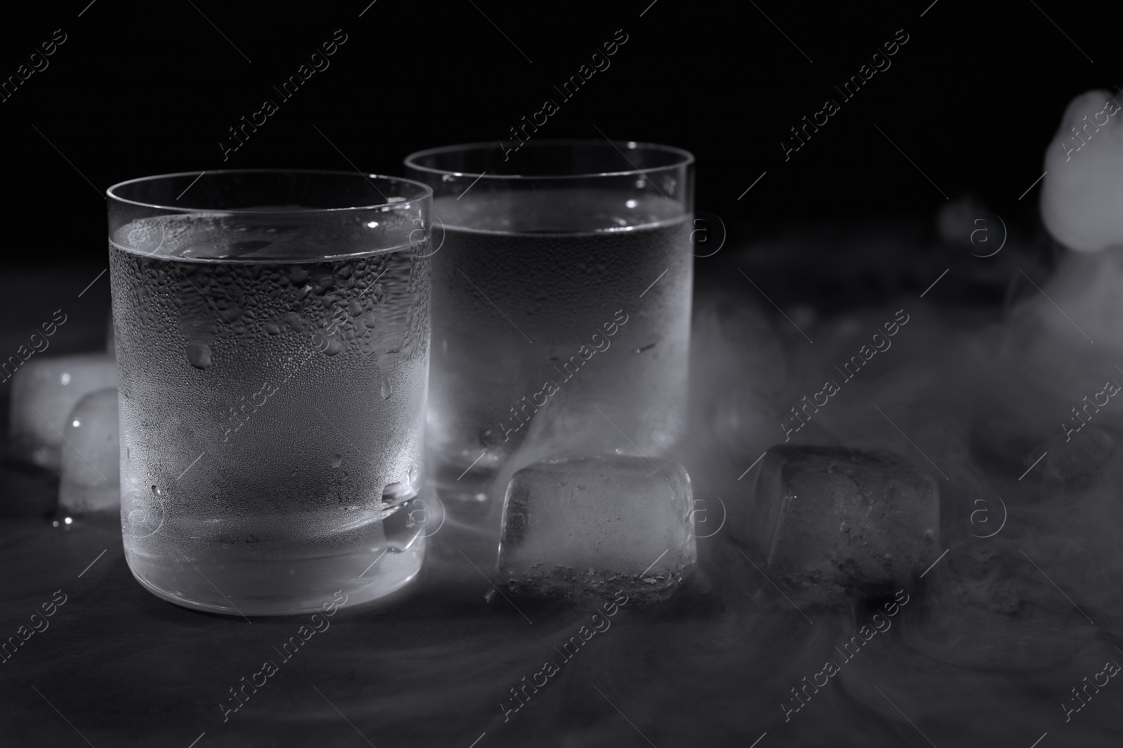 Photo of Vodka in shot glasses with ice on table against black background, closeup