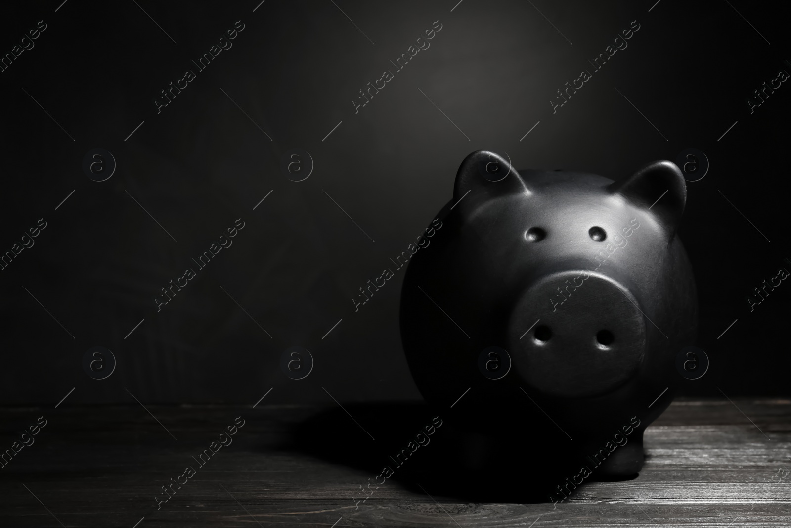 Photo of Black piggy bank on table against dark background with space for text. Poverty concept
