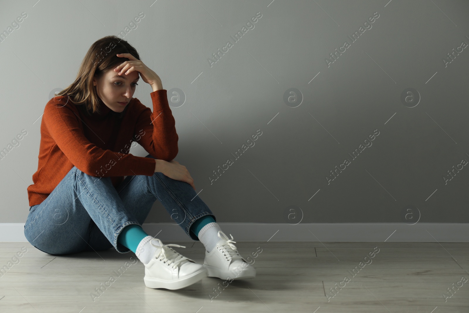 Photo of Sad young woman sitting on floor near grey wall indoors, space for text