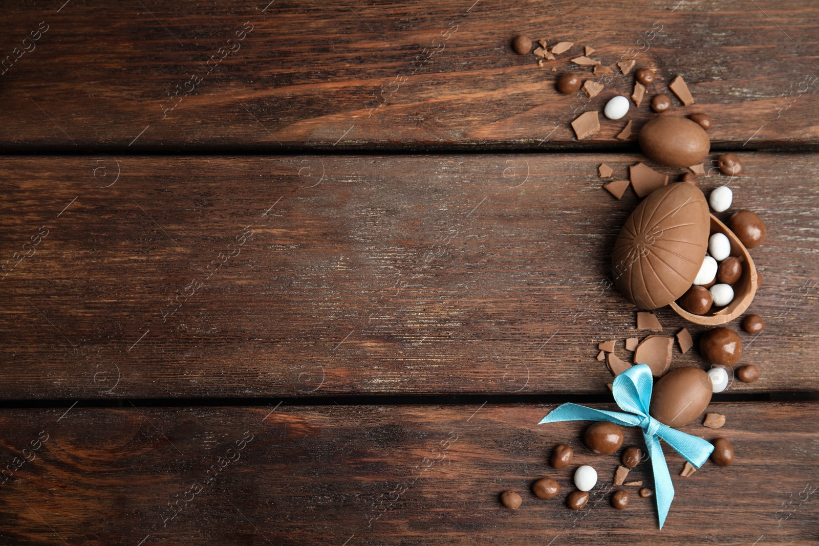 Photo of Flat lay composition with delicious chocolate Easter eggs and candies on wooden table. Space for text