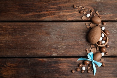 Flat lay composition with delicious chocolate Easter eggs and candies on wooden table. Space for text