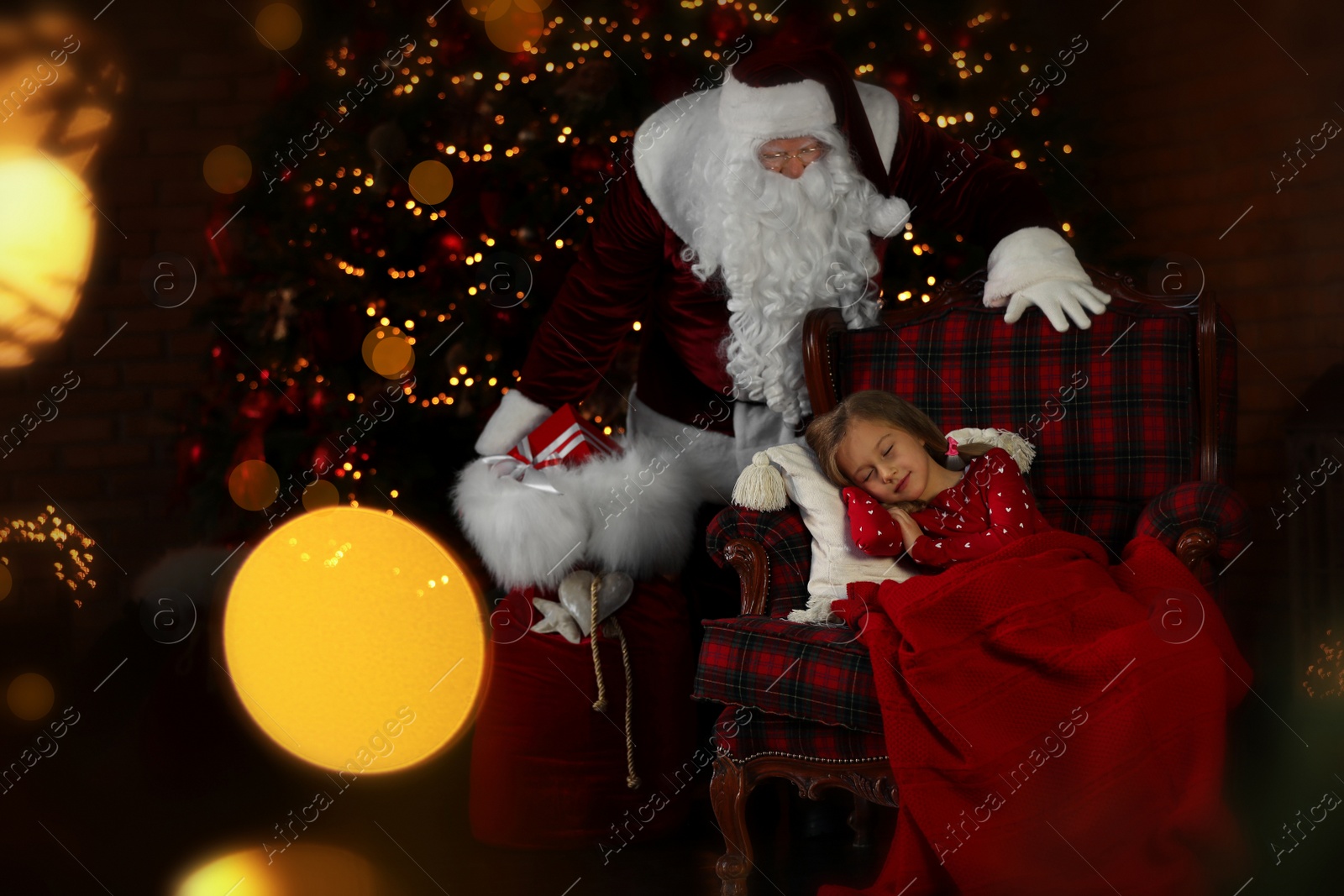 Photo of Santa Claus with Christmas gifts standing near sleeping little girl indoors