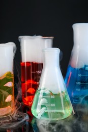 Photo of Laboratory glassware with colorful liquids and steam on black background. Chemical reaction