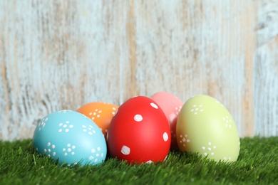 Colorful painted Easter eggs on green grass against wooden background