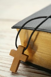 Photo of Christian cross and Bible on white wooden table, closeup