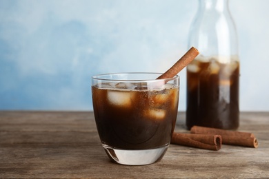 Photo of Glass of coffee with ice cubes on table against color background