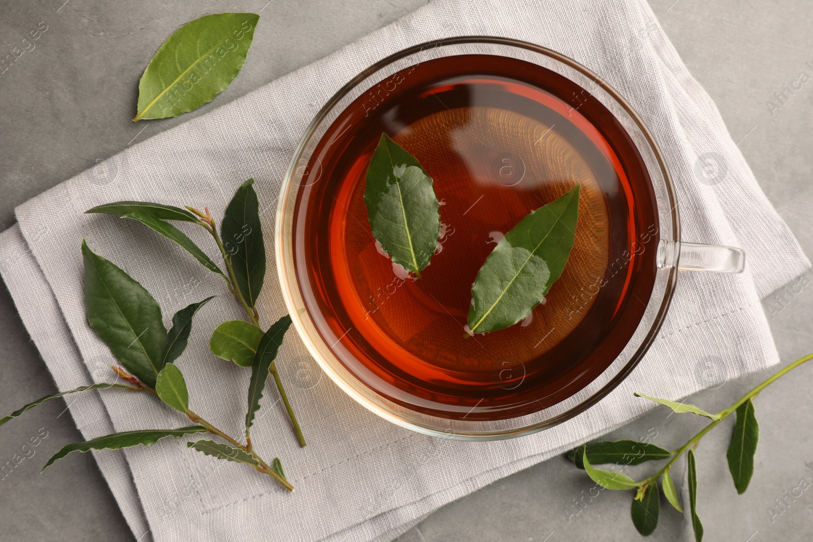 Photo of Cup of freshly brewed tea with bay leaves on grey table, flat lay