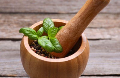 Photo of Mortar with peppercorns and basil on wooden table, closeup