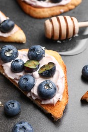 Photo of Tasty sandwiches with cream cheese, honey and berries on grey table, closeup
