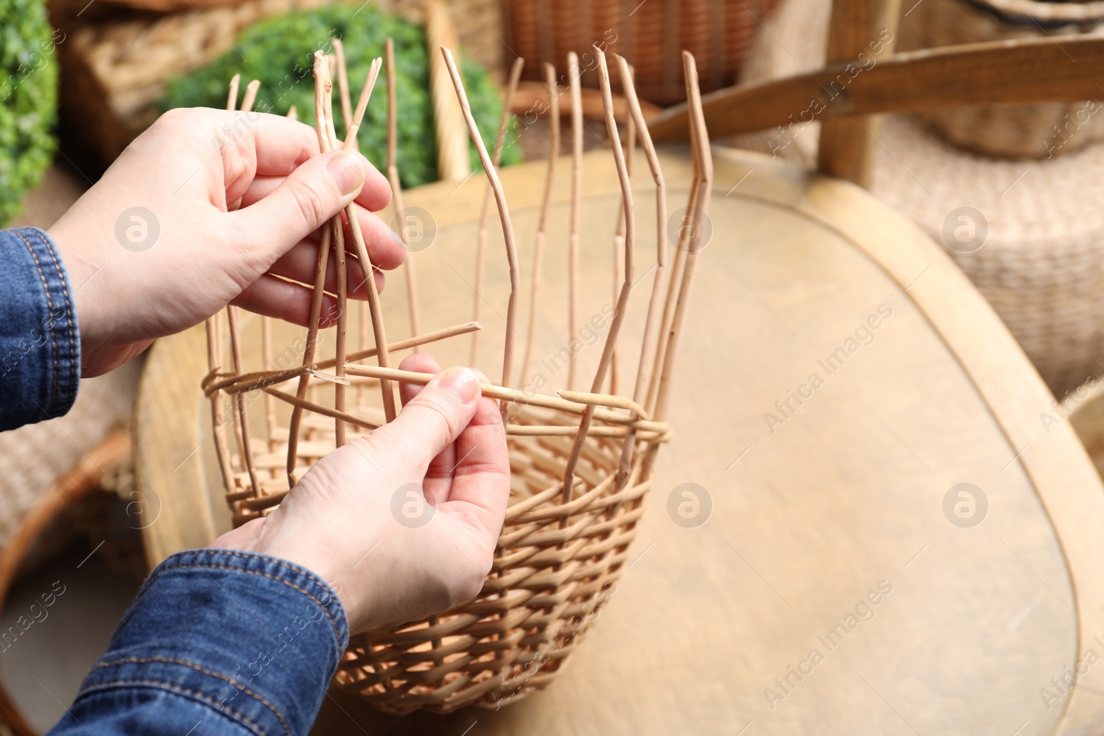 Photo of Woman weaving wicker basket indoors, closeup view