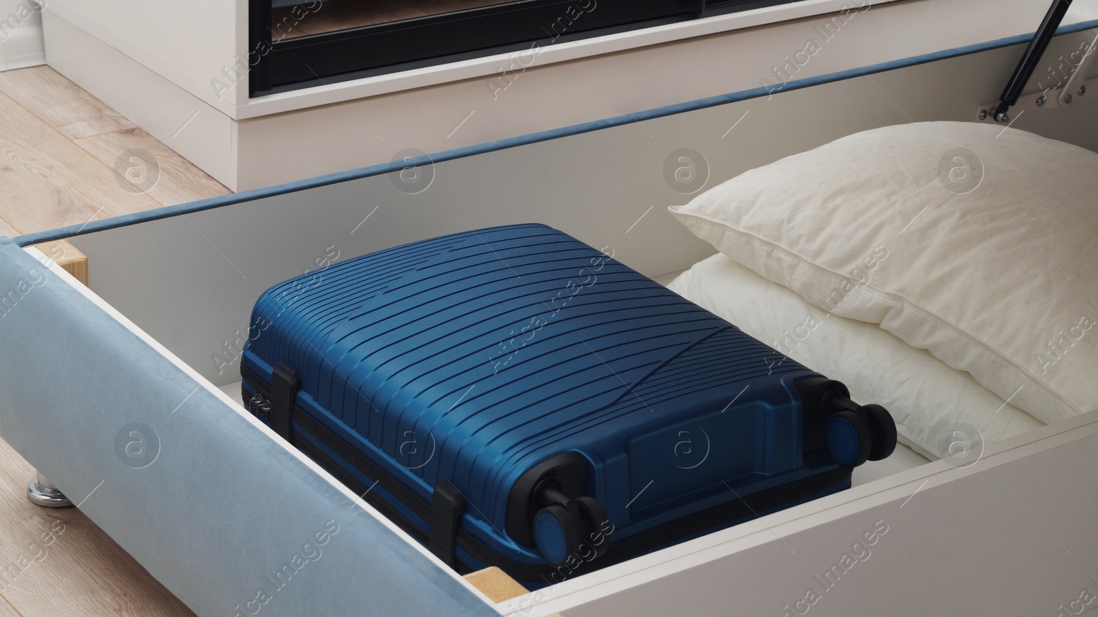 Photo of Storage drawer under bed with blue suitcase and white pillows indoors