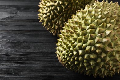 Photo of Ripe durians on black wooden table, closeup. Space for text