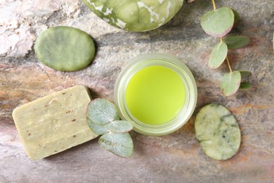 Jar of cream, spa stones, soap and eucalyptus branches on textured table, flat lay. Body care product