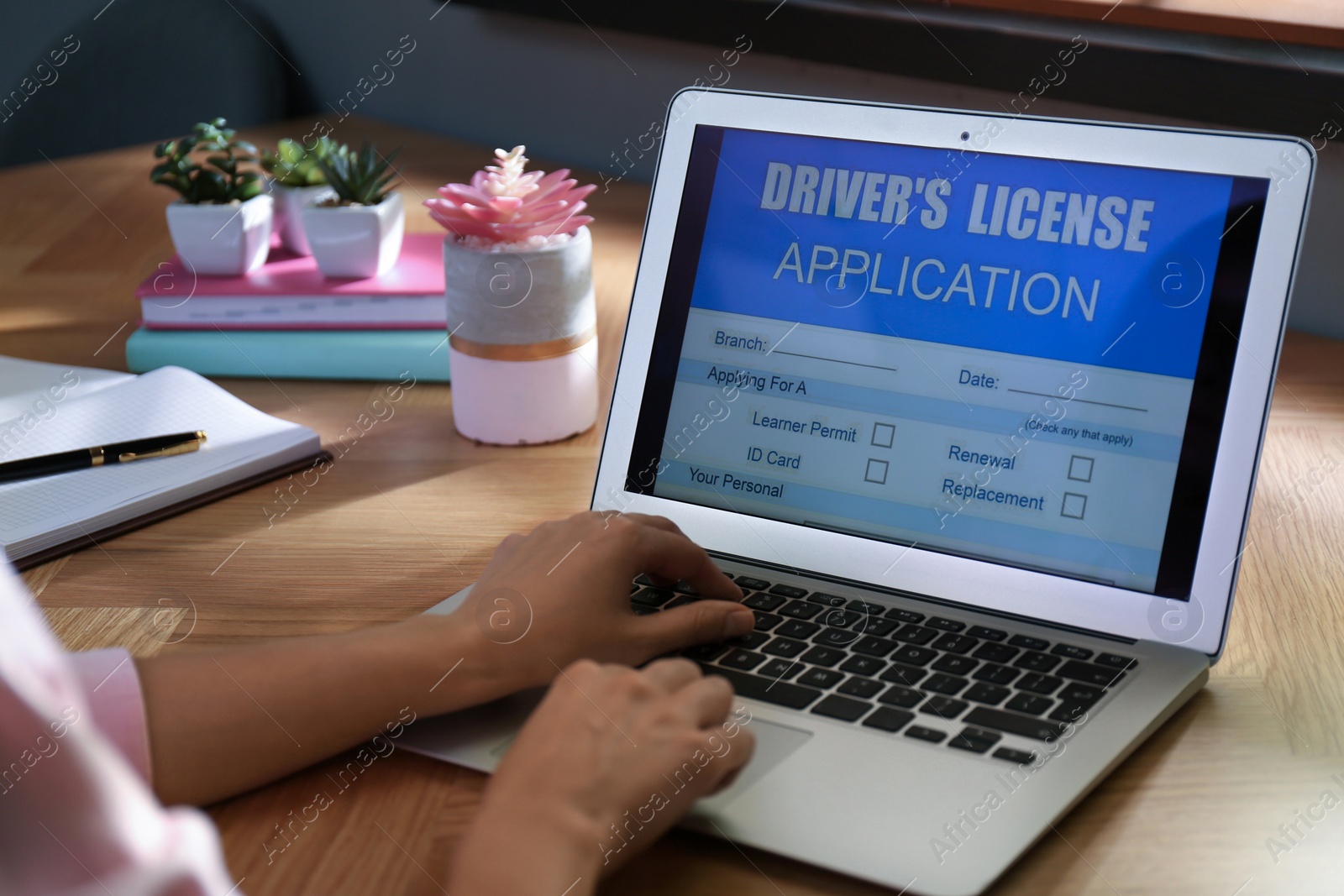 Photo of Woman using laptop to fill driver's license application form at table in office, closeup