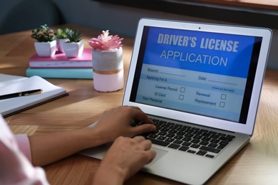 Woman using laptop to fill driver's license application form at table in office, closeup