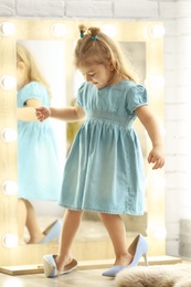 Cute little girl wearing high heeled shoes at home