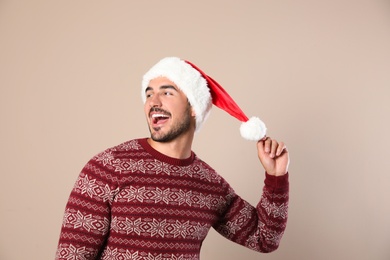 Photo of Happy young man in Christmas sweater and Santa hat on beige background