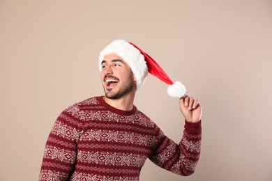 Happy young man in Christmas sweater and Santa hat on beige background