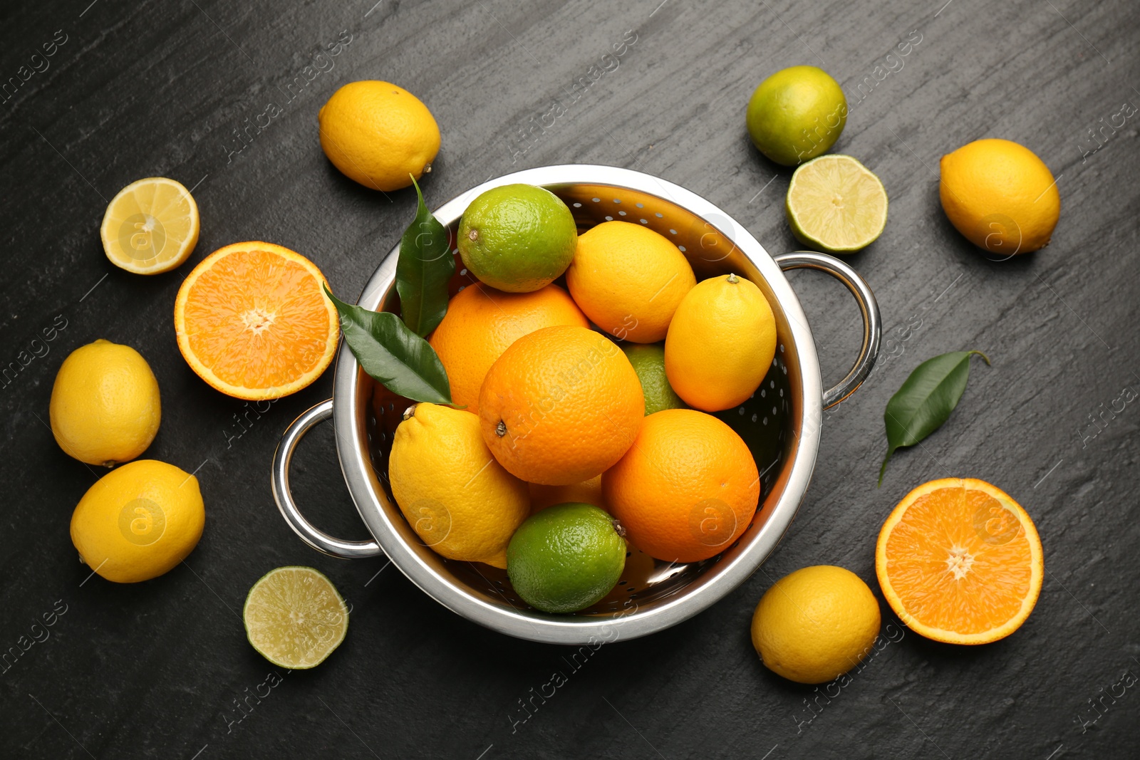 Photo of Fresh citrus fruits in colander on dark textured table, flat lay