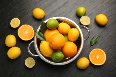 Photo of Fresh citrus fruits in colander on dark textured table, flat lay