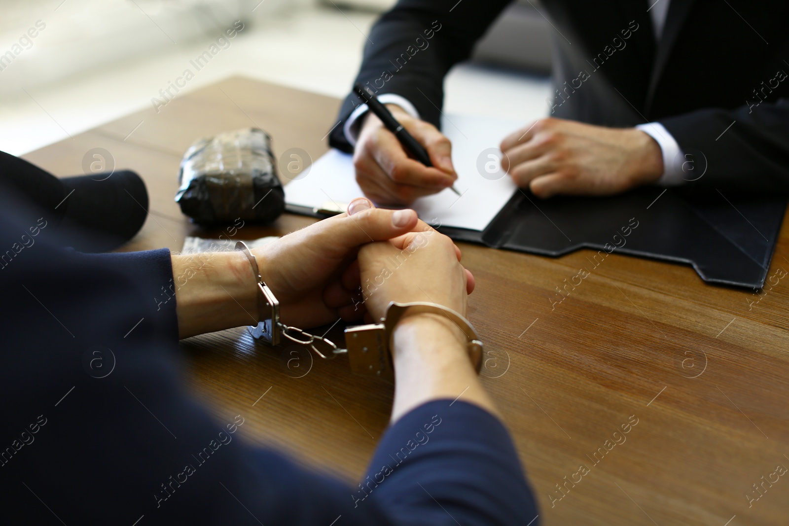 Photo of Police officer interrogating criminal in handcuffs at desk indoors