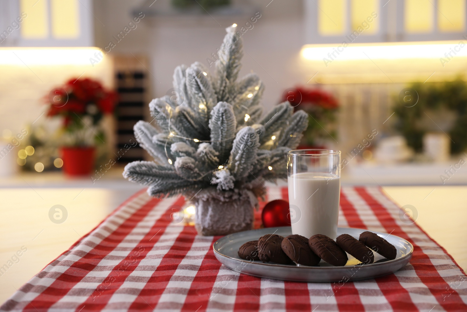 Photo of Glass of milk and chocolate cookies near little Christmas tree on table indoors