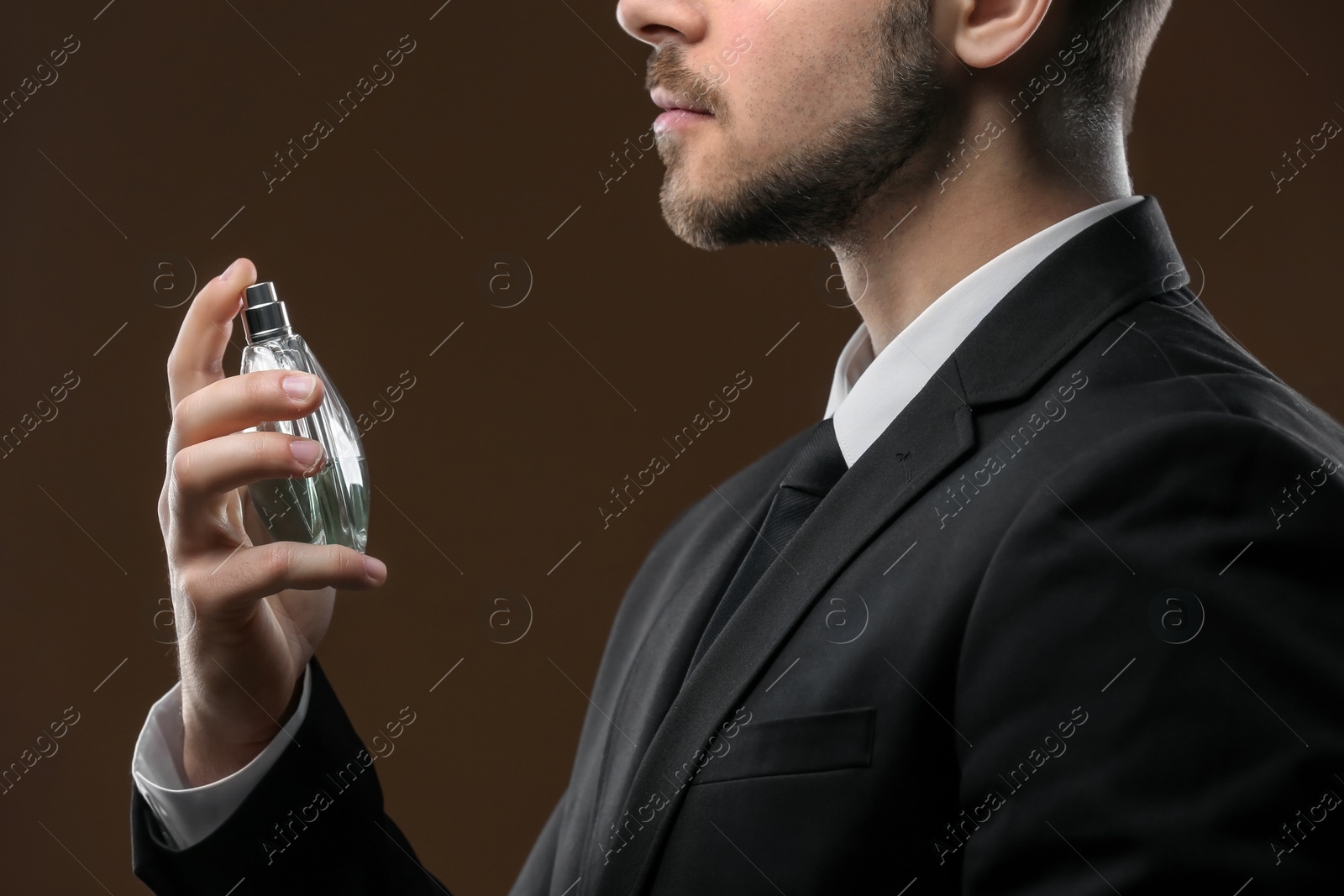 Photo of Handsome man in suit using perfume on dark background, closeup