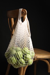 Green apples in net bag hanging on wooden chair against black background