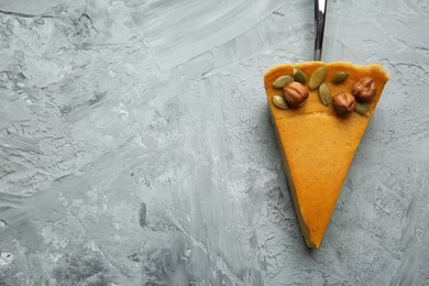 Photo of Cake server with piece of delicious pie with hazelnuts and pumpkin seeds on grey textured table, top view. Space for text