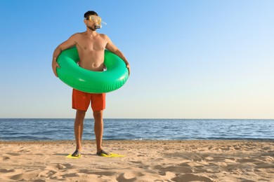 Man with flippers, inflatable ring and goggles on sea beach. Space for text