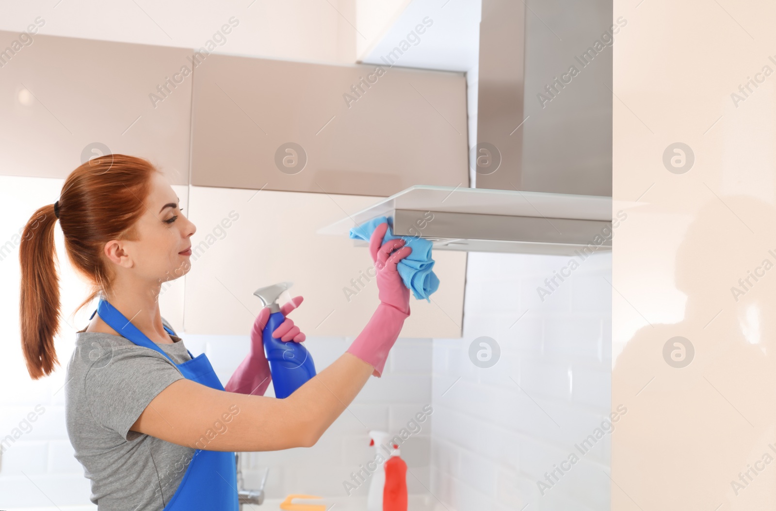 Photo of Woman in protective gloves cleaning kitchen with rag, indoors