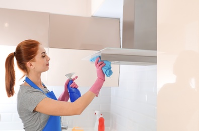 Woman in protective gloves cleaning kitchen with rag, indoors