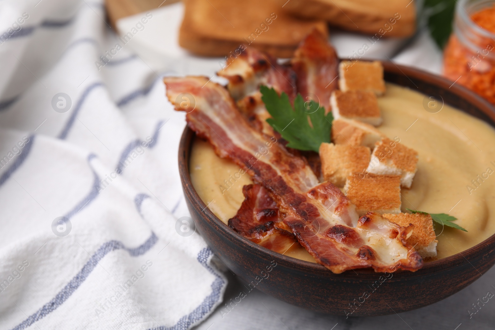 Photo of Delicious lentil soup with bacon and parsley in bowl on table, closeup