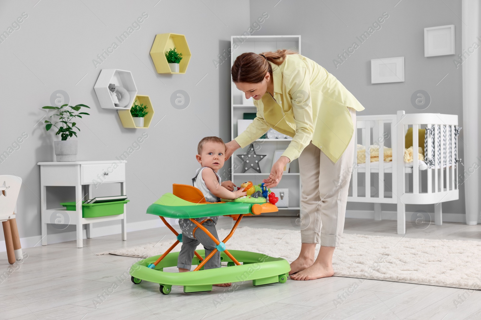 Photo of Mother and her little son at home. Cute baby making first steps with toy walker