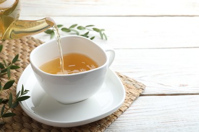 Photo of Pouring aromatic eucalyptus tea into cup on white wooden table. Space for text