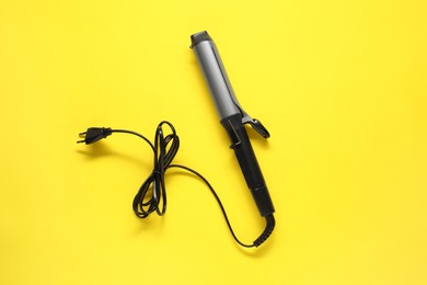 Photo of Curling iron on yellow background, top view