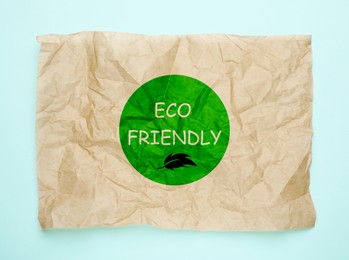 Image of Sheet of crumpled paper with phrase Eco Friendly on light blue background, top view