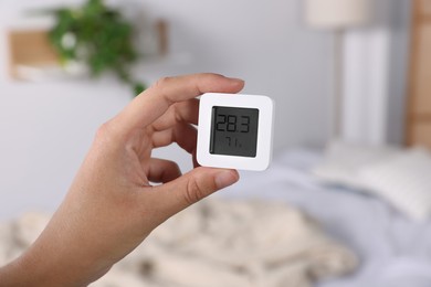 Photo of Woman holding digital hygrometer with thermometer indoors, closeup