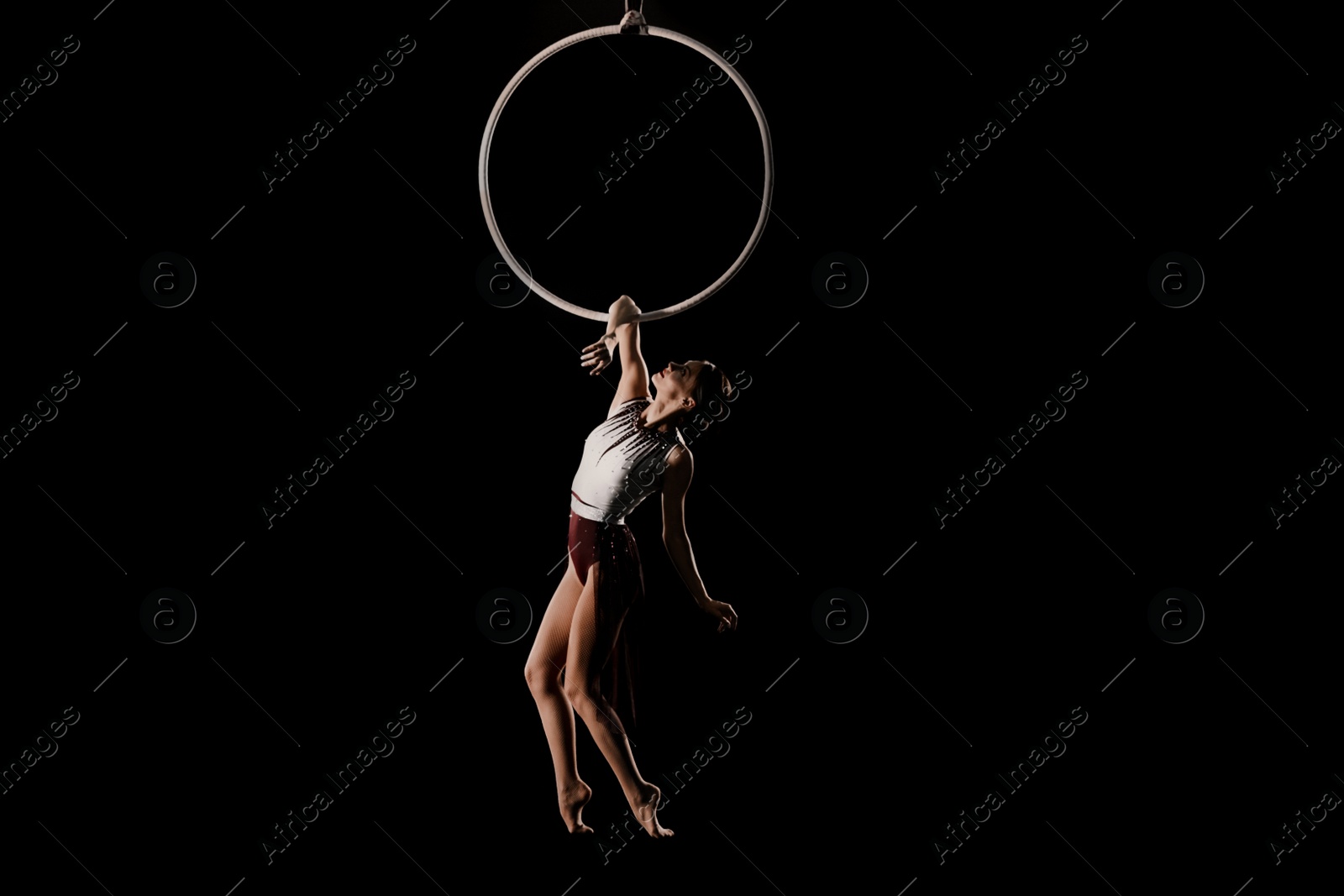 Photo of Young woman performing acrobatic element on aerial ring indoors