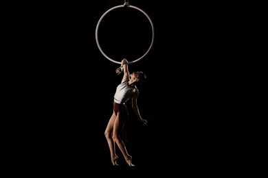 Photo of Young woman performing acrobatic element on aerial ring indoors