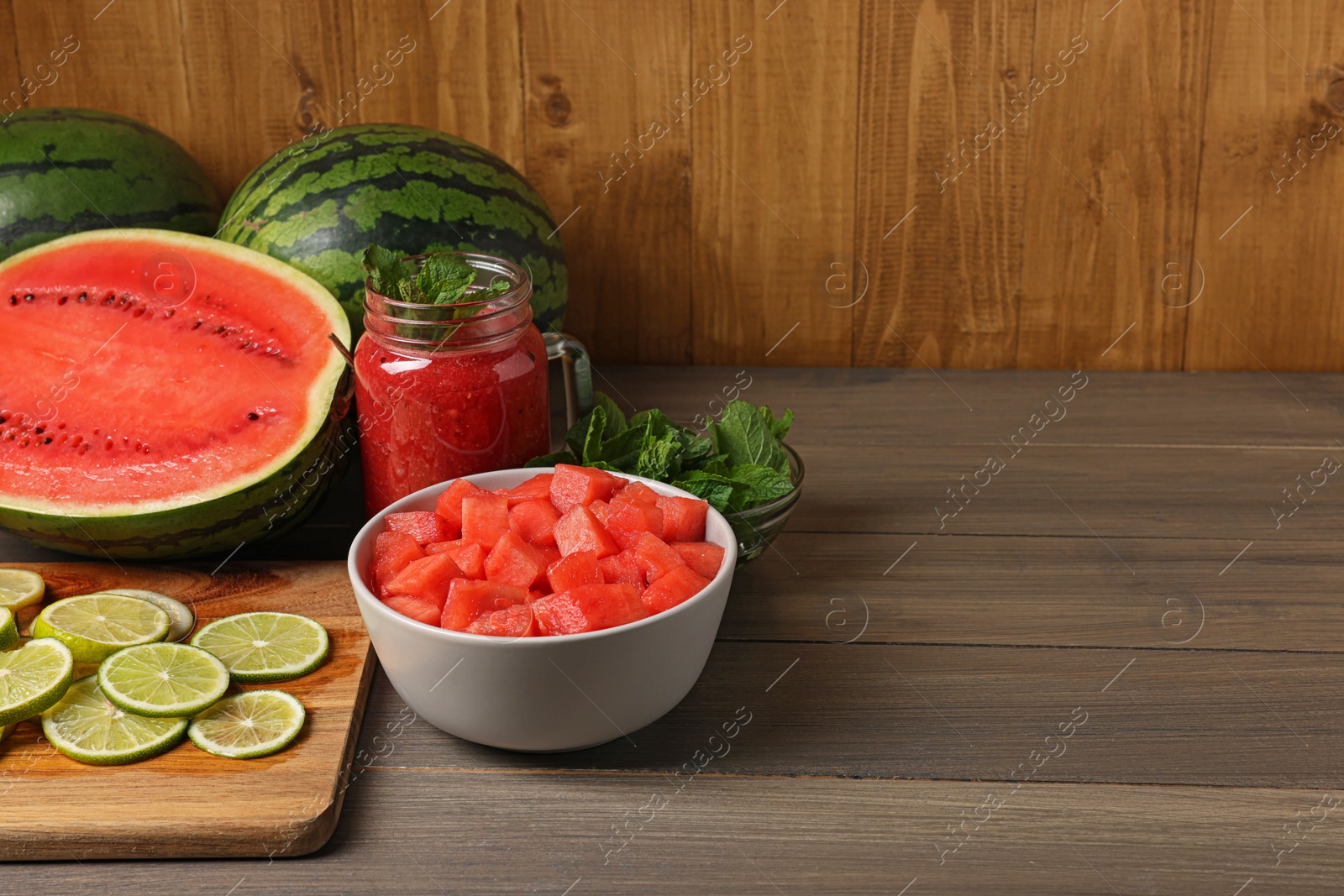 Photo of Tasty watermelon drink with lime and fresh ingredients on wooden table, space for text