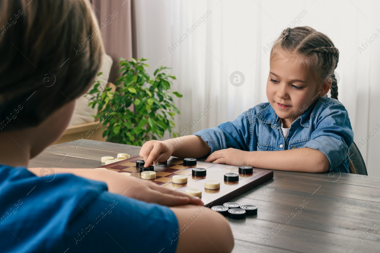 Photo of Cute boy playing checkers with little girl at table in room, closeup