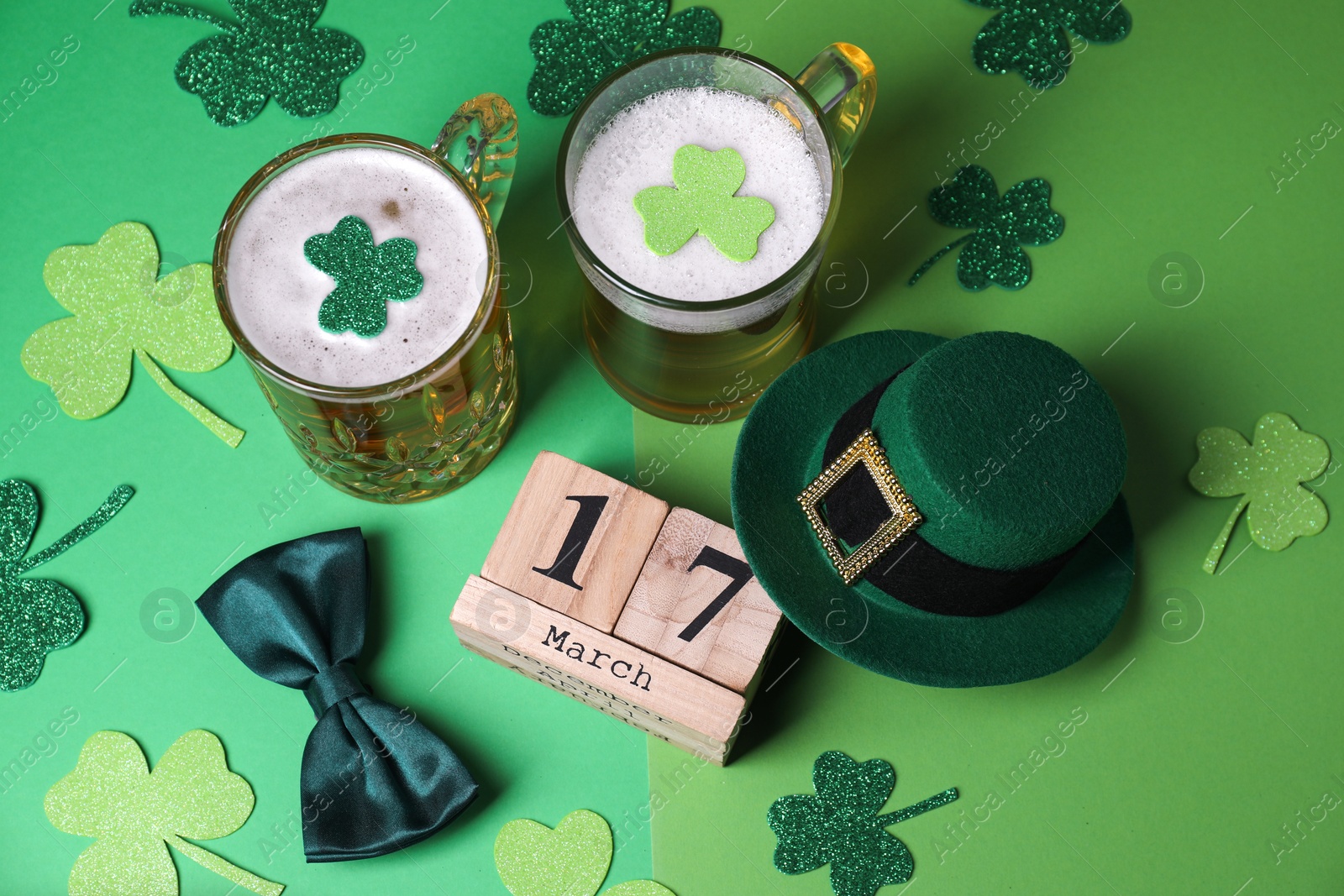 Photo of St. Patrick's day party on March 17. Green beer, leprechaun hat, bowtie, wooden block calendar and decorative clover leaves on green background, above view