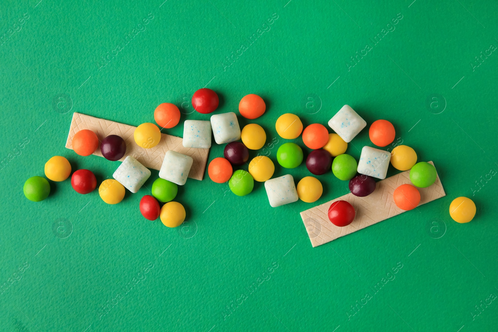 Photo of Different tasty chewing gums on green background, flat lay