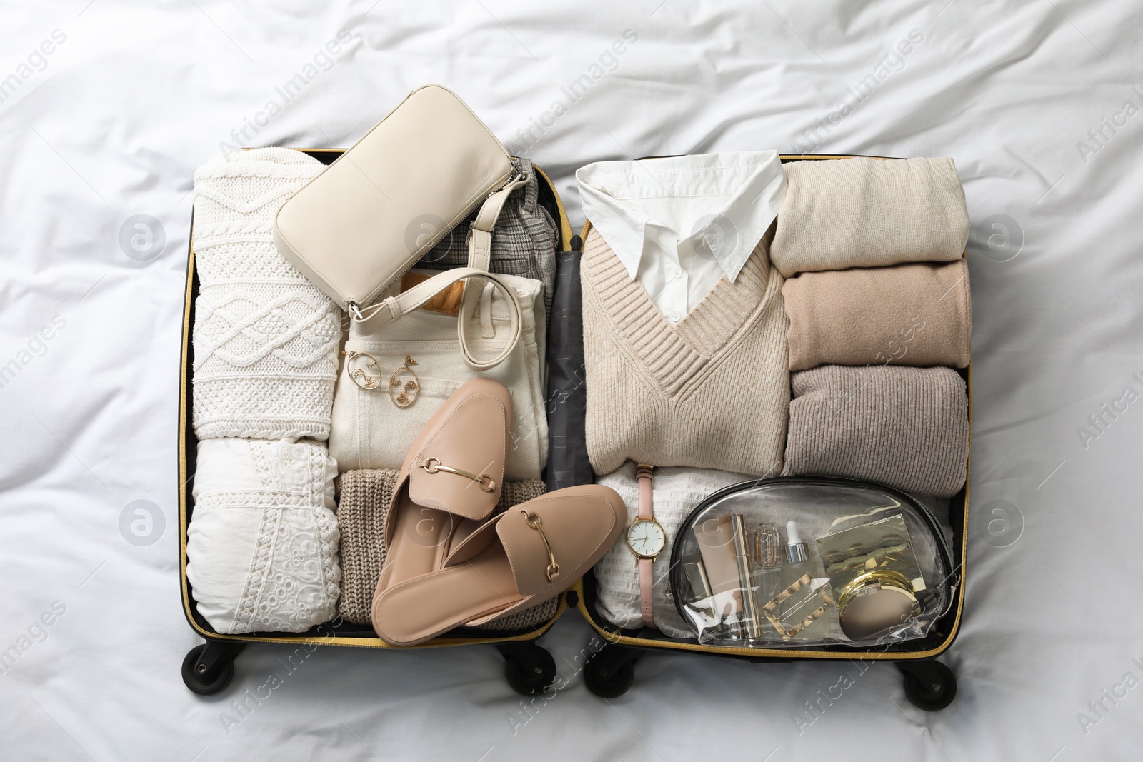 Photo of Open suitcase with folded clothes, shoes and accessories on bed, top view